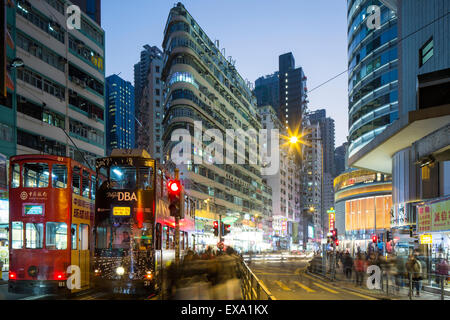 Cina, Hong Kong, Hong Kong Tramways street cars fermato al semaforo in centro città incandescente sotto le luci di strada al tramonto su Foto Stock