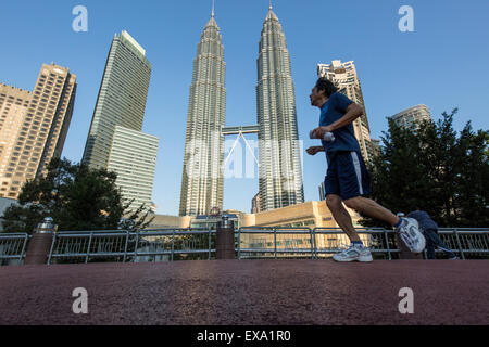 Malaysia, Kuala Lumpur, basso angolo di visione dell'uomo jogging sul sentiero nel parco pubblico sotto 88 storia alte torri Petronas grattacieli Foto Stock