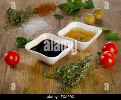 Medicazione ingredienti su un sfondo rustico. Olio d'oliva, aceto balsamico, erbe aromatiche, sale e pepe. Messa a fuoco selettiva Foto Stock