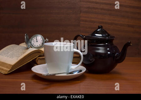 Tazze da tè con teiera, libri e il vecchio orologio da tasca sul tavolo di legno. Messa a fuoco selettiva. Foto Stock