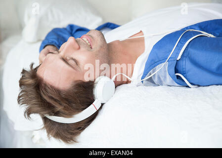 Uomo disteso sul letto ascoltando musica con le cuffie Foto Stock