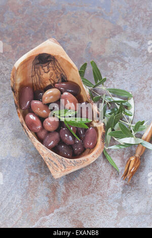 Misto di olive oleoso in legno d'olivo ciotola e rametto di oliva..Macro , il fuoco selettivo, copia spazio, vista dall'alto Foto Stock