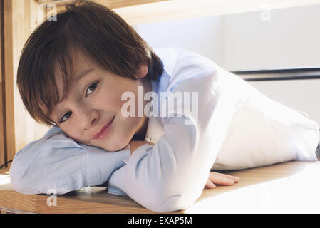 Ragazzo appoggiato la testa sulle braccia, sorridente, ritratto Foto Stock