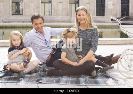 Famiglia seduti su una coperta nel parco urbano, ritratto Foto Stock