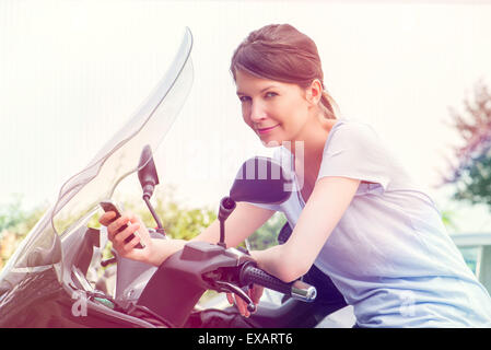 Donna appoggiata contro la motocicletta, utilizza lo smartphone Foto Stock