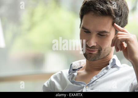 Uomo che guarda con attenzione verso il basso con il dito premuto contro il tempio Foto Stock