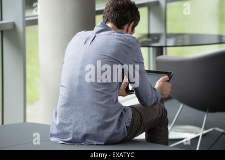 Uomo seduto da solo, guardando a tavoletta digitale, vista posteriore Foto Stock