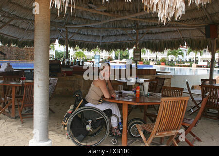 Donna che utilizza una sedia a rotelle a un pool bar in Belize Foto Stock