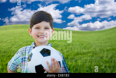 Carino sorridente ragazzo giovane azienda Pallone da calcio in erba verde nel Parco. Foto Stock