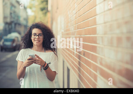 Giovani belle marocchino donna ricci utilizza lo smartphone nella città Foto Stock