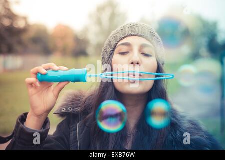 Giovane bella bruna donna soffiare bolle sapone in città Foto Stock