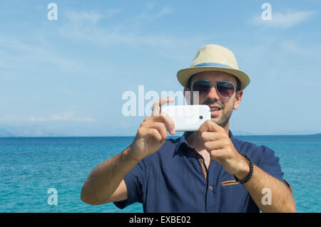 Uomo di scattare le foto con il suo telefono cellulare al mare Foto Stock