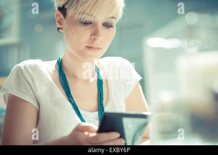 Giovane e bella bionda capelli corti hipster donna utilizzando tablet presso il cafe Foto Stock