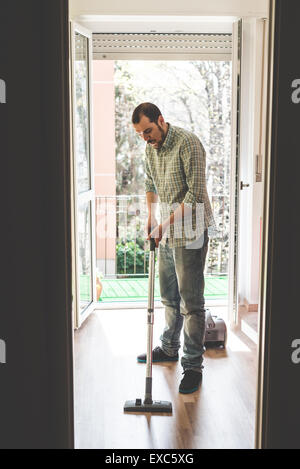 Bello elegante uomo utilizzando hoover a casa Foto Stock