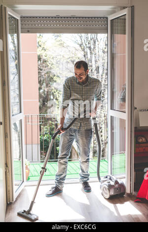 Bello elegante uomo utilizzando hoover a casa Foto Stock