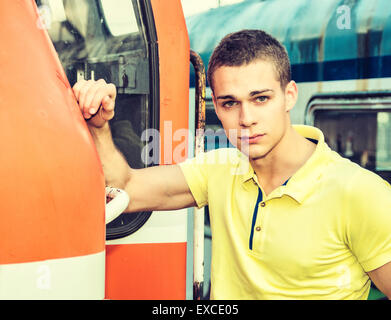 Bel giovane uomo in giallo Polo shirt nella parte anteriore del treno, guardando la fotocamera. Close-up shot Foto Stock