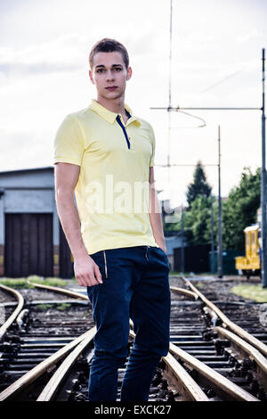 Attraente giovane uomo in piedi sulla ferrovia, indossando il giallo Polo shirt e jeans, guardando la fotocamera Foto Stock