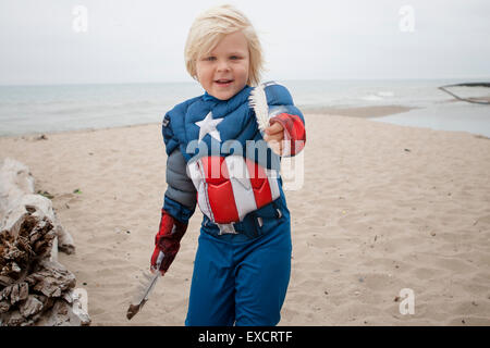 A quattro anni di vecchio ragazzo che indossa un capitano America costume può contenere fino a due piume di uccello su di una spiaggia di sabbia sul Lago Michigan. Foto Stock