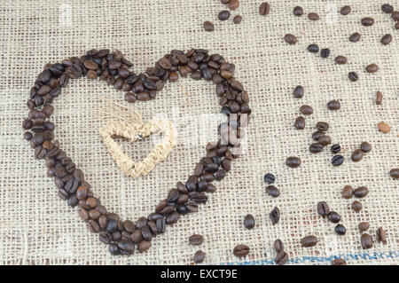 A forma di cuore i grani di caffè posto su un sacco di caffè con sparsi grani di caffè Foto Stock