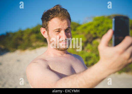 Bello redhead uomo barbuto prendendo selfie con lo smartphone in spiaggia in estate Foto Stock