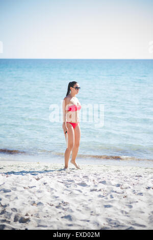 Giovane bella bruna donna che indossa il costume da bagno e occhiali da sole in estate in spiaggia con la racchetta Foto Stock