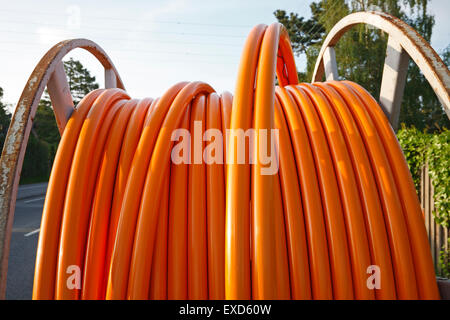 Il cavo arancione per le connessioni a banda larga su un rullo avvolgicavo in acciaio su una strada suburbana. Foto Stock