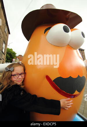 Belper, Derbyshire, Regno Unito. 12 Luglio, 2015. Brii Matheson, 8,da Belper abbracci un gigante Mr Potato Head che ha ri-apparve in Derbyshire città. La 7ft statua in fibra di vetro è stato regalato a Belper nel 2001 dalla sua città gemelle, Pawtucket, Rhode Island, Stati Uniti d'America. Dopo essere stato ribattezzato "onstrosity" da parte di alcuni locali, il carattere divisivo realizzati titoli nazionali. È stato soggetto ad atti vandalici e bandito. Ora il spud è stata spruced fino da un gruppo locale di giovani e svelato a Belper's Food festival di oggi. Credito: Deborah Vernon/Alamy Live News Foto Stock
