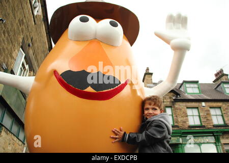Belper, Derbyshire, Regno Unito. 12 Luglio, 2015. Tre-anno-vecchio Darwyn Reed da Belper abbracci un gigante Mr Potato Head che ha ri-apparve in Derbyshire città. La 7ft statua in fibra di vetro è stato regalato a Belper nel 2001 dalla sua città gemelle, Pawtucket, Rhode Island, Stati Uniti d'America. Dopo essere stato ribattezzato "onstrosity" da parte di alcuni locali, il carattere divisivo realizzati titoli nazionali. È stato soggetto ad atti vandalici e bandito. Ora il spud è stata spruced fino da un gruppo locale di giovani e svelato a Belper's Food festival di oggi. Credito: Deborah Vernon/Alamy Live News Foto Stock