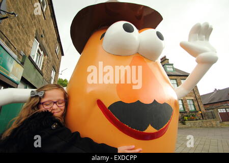 Belper, Derbyshire, Regno Unito. 12 Luglio, 2015. Brii Matheson, 8,da Belper abbracci un gigante Mr Potato Head che ha ri-apparve in Derbyshire città. La 7ft statua in fibra di vetro è stato regalato a Belper nel 2001 dalla sua città gemelle, Pawtucket, Rhode Island, Stati Uniti d'America. Dopo essere stato ribattezzato "onstrosity" da parte di alcuni locali, il carattere divisivo realizzati titoli nazionali. È stato soggetto ad atti vandalici e bandito. Ora il spud è stata spruced fino da un gruppo locale di giovani e svelato a Belper's Food festival di oggi. Credito: Deborah Vernon/Alamy Live News Foto Stock