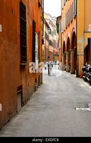 Un uomo in bicicletta giù per una strada stretta con edifici rosso nella città di Bologna, Italia Foto Stock