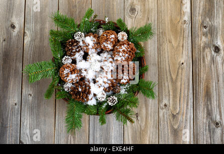 Cesto Natalizio riempito con pino rami, coni e la neve su rustiche tavole in legno. Foto Stock