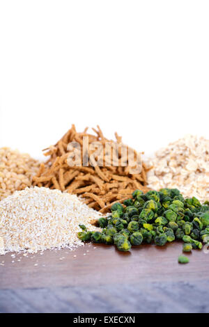 Pila di sano ad alto contenuto di fibre prebiotiche comprendente grani di crusca di frumento cereali, fiocchi di avena e di orzo perlato, su rustiche in legno scuro tabella Foto Stock