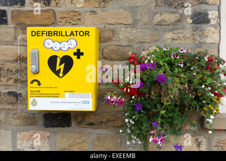 Defibrillatore cardiaco di salvataggio Attrezzature per arresto cardiaco con il blocco di codice per uso pubblico in una città con cesto fiorito in Inghilterra Foto Stock