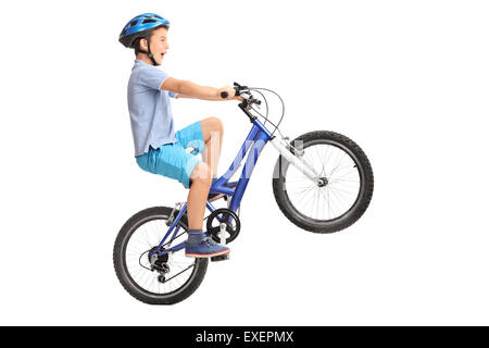 Colpo di profilo di un ragazzino con casco blu facendo un'impennata su un piccolo blu bike isolati su sfondo bianco Foto Stock