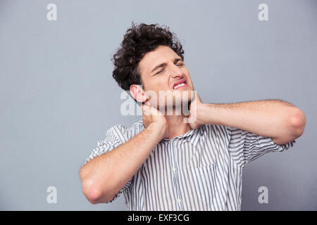 Ritratto di un giovane uomo di avere mal di collo su sfondo grigio Foto Stock
