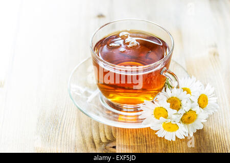 Tazza di tè con i fiori di camomilla sul rustico sfondo di legno Foto Stock