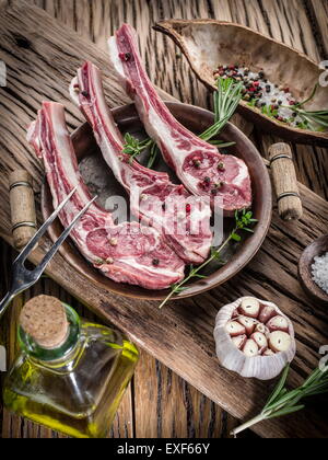 Materie costolette di agnello con aglio ed erbe aromatiche sul vecchio tavolo in legno. Foto Stock