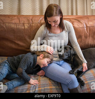 Madre e figlio rilassante sul divano di casa con pet labrador Foto Stock