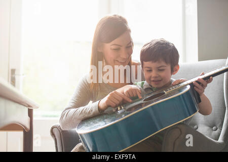 Ragazzo seduto sulla madre di giro in camera da sole e imparare a suonare la chitarra Foto Stock