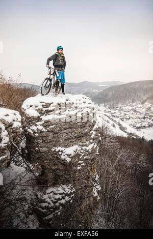 Giovane maschio mountain biker sulla cima coperta di neve rock formazione Foto Stock