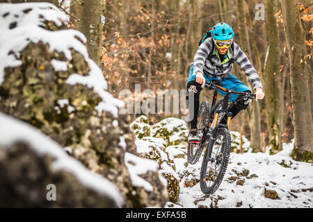 Giovane maschio mountain biker accelerando sulla coperta di neve rocce in foresta Foto Stock