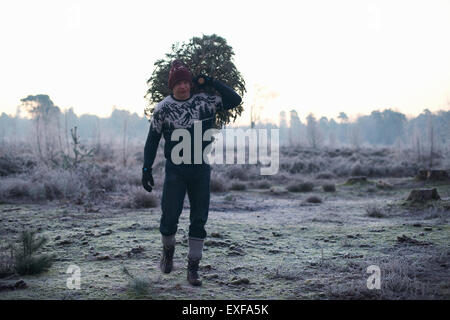Boscaiolo con abete sulla sua spalla nel bosco Foto Stock