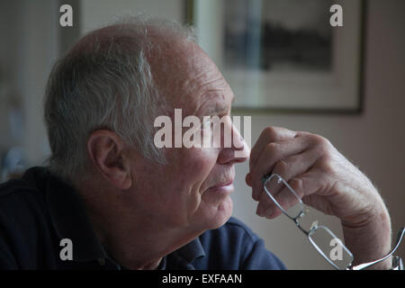 L'uomo anziano, tenendo occhiali, guardando fuori della finestra Foto Stock