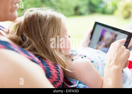 Figlia seduti sulla madre di giro utilizzando tavoletta digitale Foto Stock