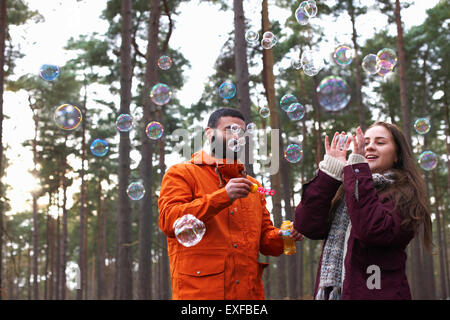 Coppia giovane soffiare bolle nella foresta Foto Stock