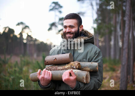 Giovane uomo a raccogliere i log per il fuoco nella foresta Foto Stock