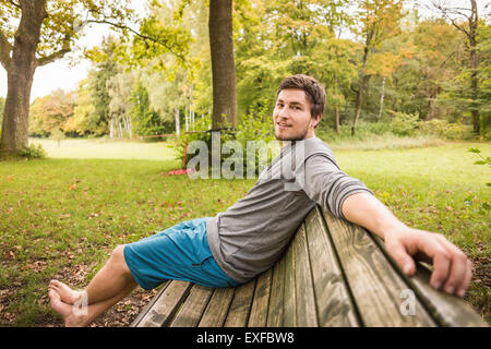 Ritratto di barefoot giovane uomo seduto su una panchina nel parco Foto Stock