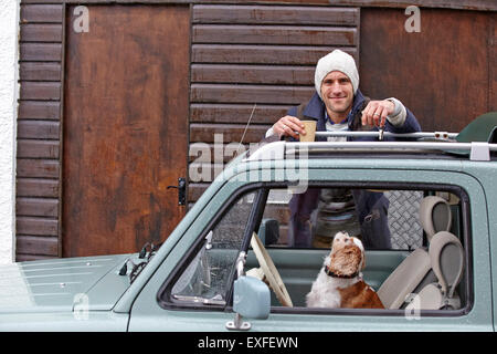 Ritratto di metà uomo adulto appoggiata contro van mentre cane guarda in alto Foto Stock