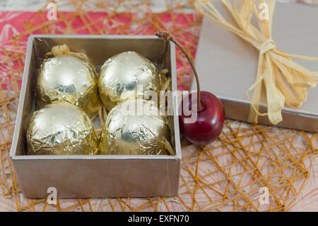 Cioccolatini avvolti in golden confezione colorata in un colore rosso presente scatola con ciliegie fresche Foto Stock