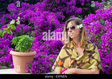 Ragazza giovane con occhiali da sole e un fiore nel suo pelo circondato da bellissimi fiori viola Foto Stock